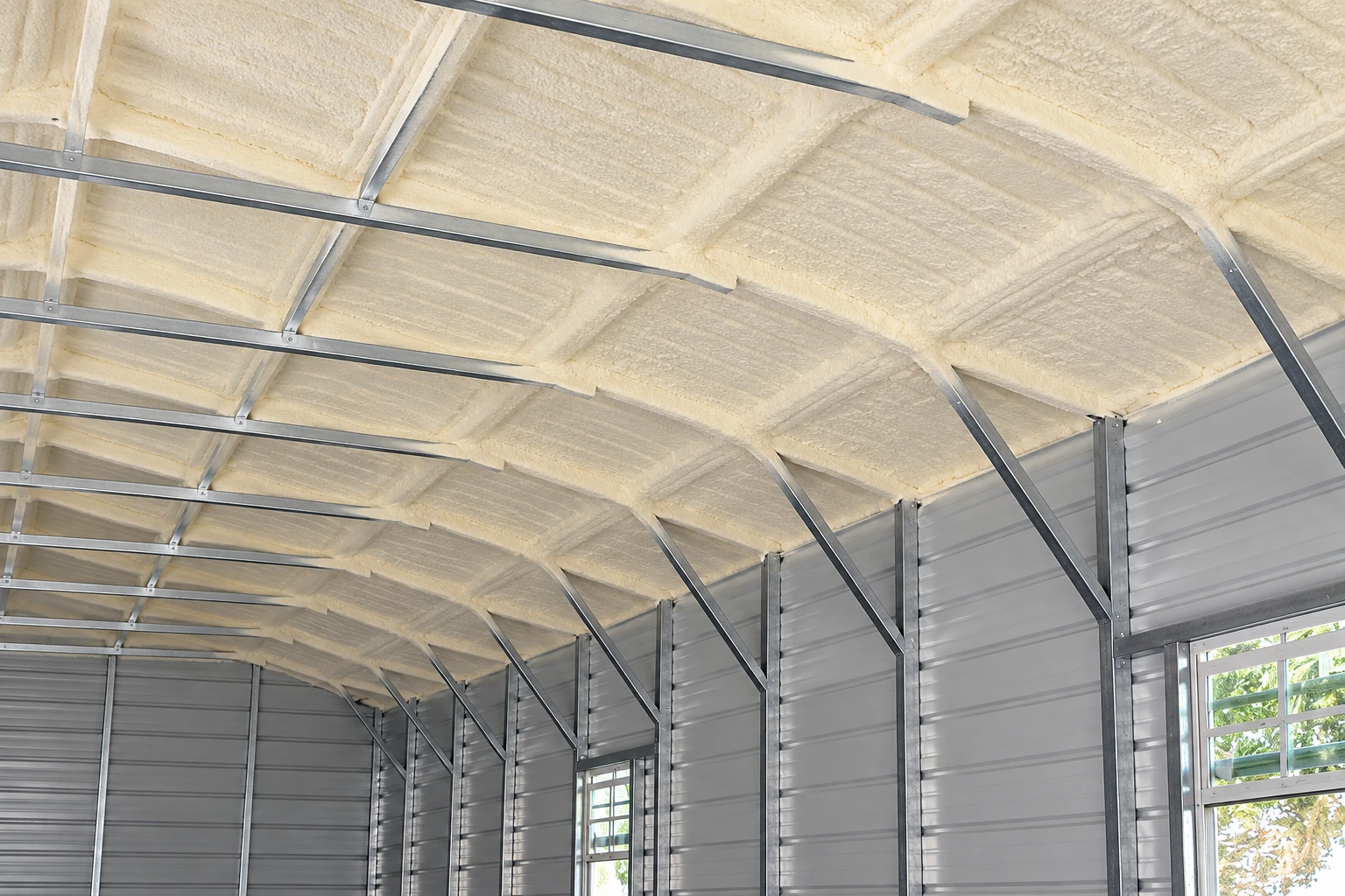 Spray foam covers the roof of a large metal-sided commercial building, supported by steel framing.