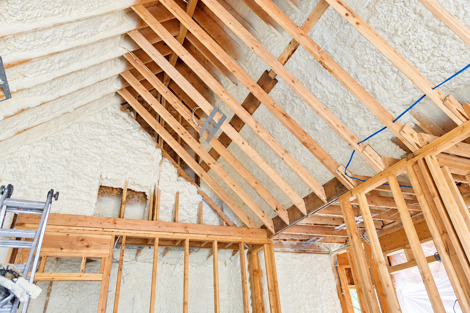 Exposed wooden roof framing and wall cavities filled with white spray foam insulation.